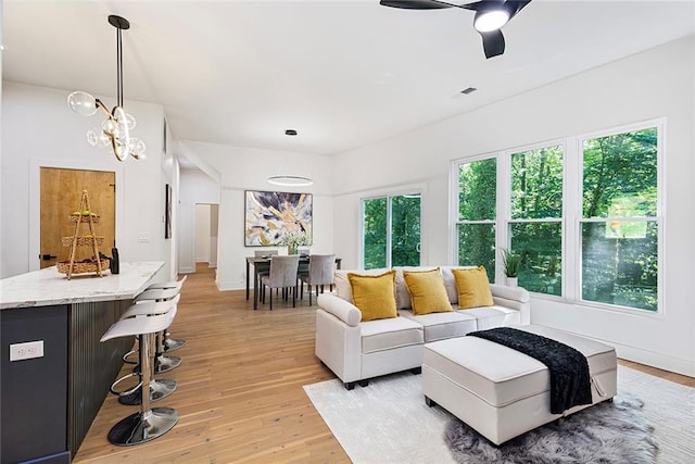 living room featuring light hardwood / wood-style floors, a wealth of natural light, and ceiling fan with notable chandelier