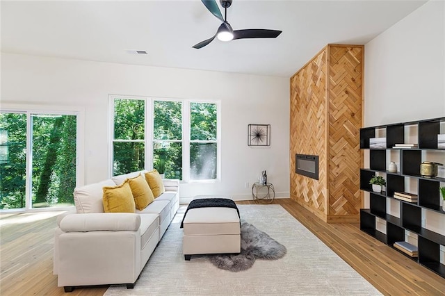 living room featuring ceiling fan, a fireplace, and light wood-type flooring