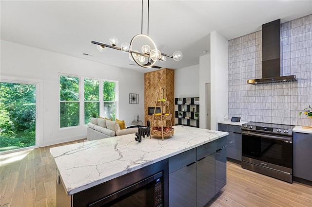 kitchen with pendant lighting, wall chimney exhaust hood, a kitchen island, a notable chandelier, and stainless steel electric range