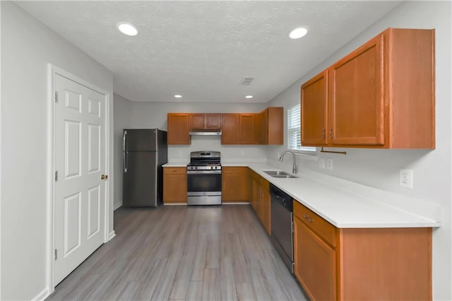 kitchen featuring a textured ceiling, light wood-type flooring, appliances with stainless steel finishes, and sink