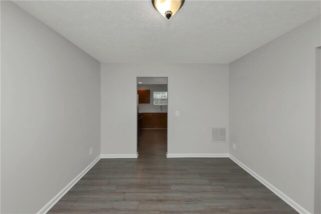 spare room featuring a textured ceiling and dark hardwood / wood-style floors