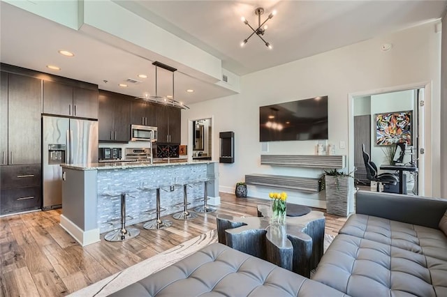 living area with visible vents, a notable chandelier, recessed lighting, light wood finished floors, and baseboards