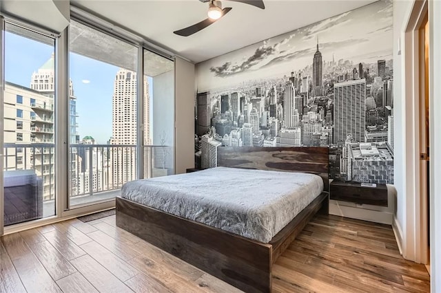 bedroom featuring wood finished floors, ceiling fan, access to exterior, floor to ceiling windows, and a city view