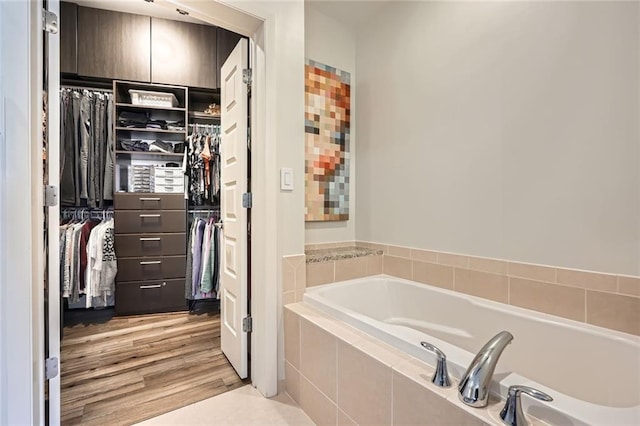 bathroom with a spacious closet, a bath, and wood finished floors