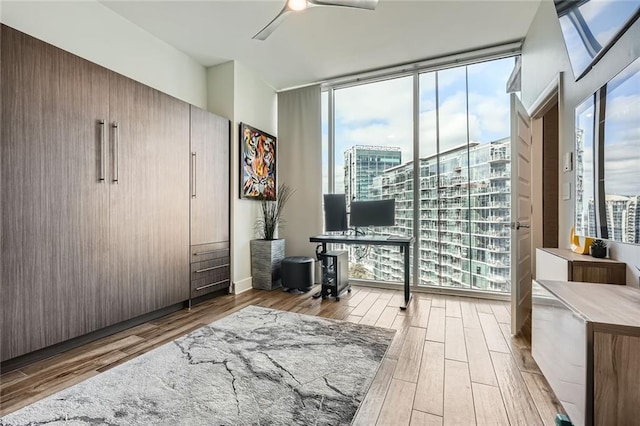 home office with a wall of windows, a healthy amount of sunlight, wood finished floors, and a ceiling fan