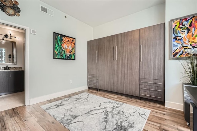 unfurnished bedroom with visible vents, light wood-type flooring, baseboards, and a sink