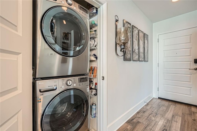 laundry area with baseboards, stacked washer and dryer, wood finished floors, and laundry area