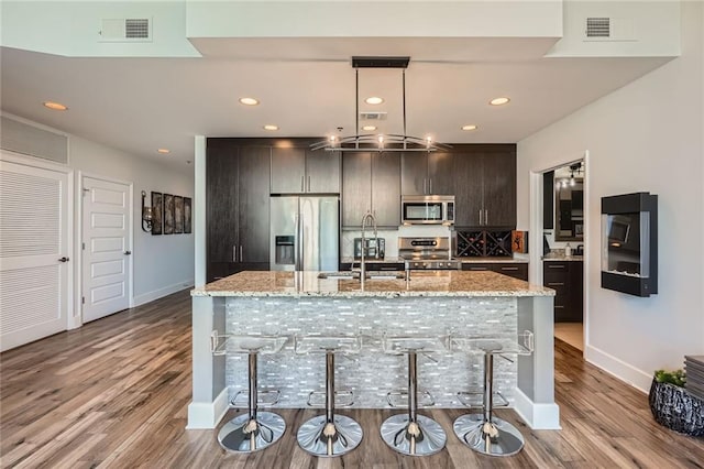 kitchen featuring a kitchen island with sink, wood finished floors, visible vents, and stainless steel appliances