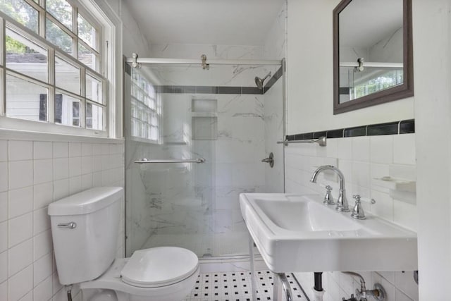 bathroom featuring sink, tile patterned floors, toilet, a shower with shower door, and tile walls