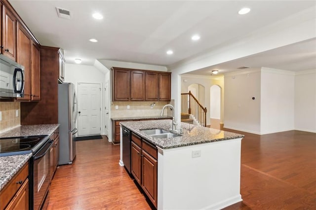 kitchen with decorative backsplash, appliances with stainless steel finishes, light wood-type flooring, a kitchen island with sink, and sink