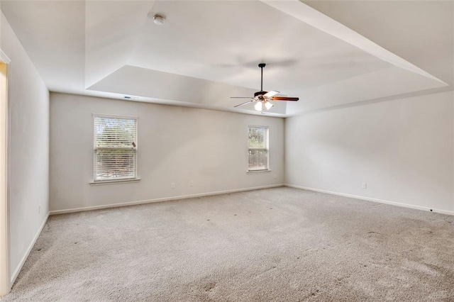 carpeted empty room featuring a raised ceiling, ceiling fan, and a healthy amount of sunlight