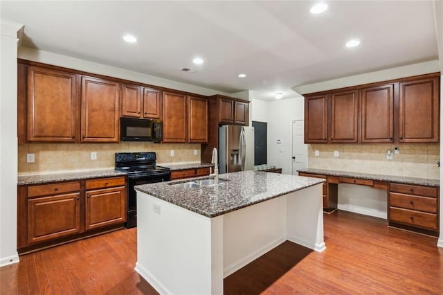 kitchen featuring stone counters, black appliances, sink, hardwood / wood-style flooring, and an island with sink