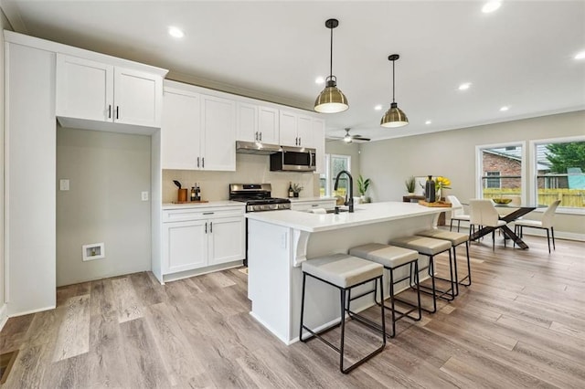 kitchen with a center island with sink, white cabinetry, stainless steel appliances, and ceiling fan