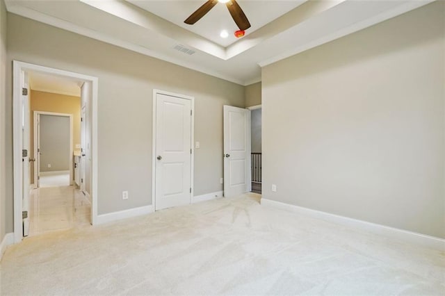 unfurnished bedroom with light carpet, a tray ceiling, ceiling fan, and ornamental molding