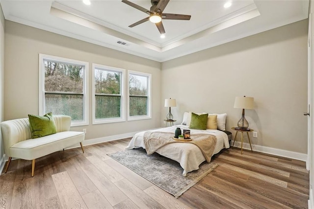 bedroom with light wood-type flooring, a raised ceiling, ceiling fan, and crown molding