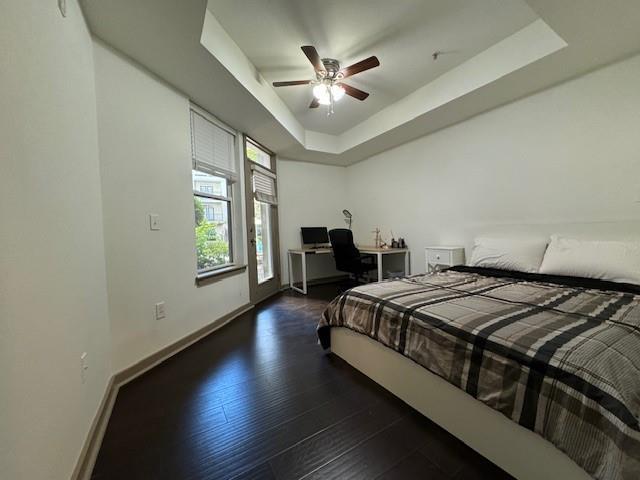 bedroom with a raised ceiling, wood finished floors, a ceiling fan, and baseboards