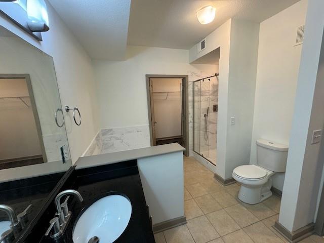 bathroom featuring toilet, a stall shower, tile patterned flooring, vanity, and a walk in closet