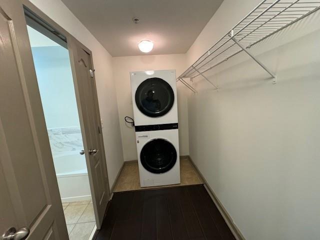 clothes washing area with stacked washing maching and dryer, baseboards, wood finished floors, and laundry area