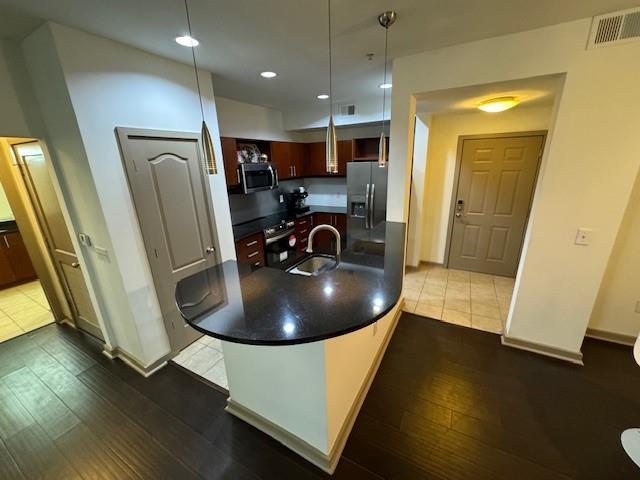 kitchen featuring stainless steel appliances, dark countertops, visible vents, a sink, and hardwood / wood-style flooring
