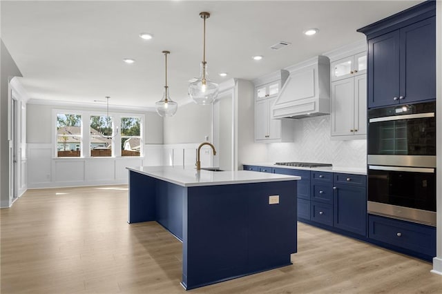 kitchen with hanging light fixtures, premium range hood, a kitchen island with sink, white cabinets, and appliances with stainless steel finishes