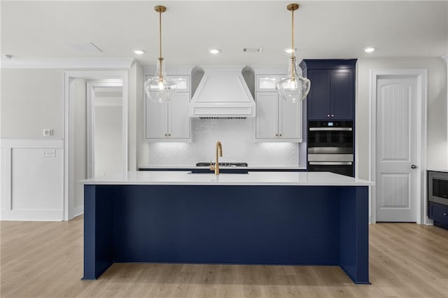 kitchen featuring pendant lighting, a center island with sink, light wood-type flooring, and custom exhaust hood