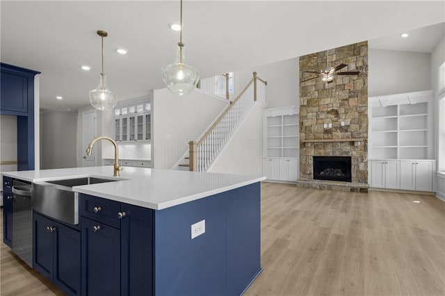 kitchen with built in shelves, sink, blue cabinetry, a stone fireplace, and an island with sink