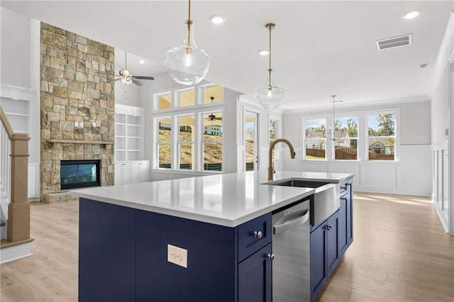 kitchen with stainless steel dishwasher, built in shelves, blue cabinetry, and a kitchen island with sink