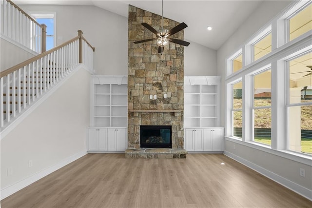 unfurnished living room featuring built in shelves, light wood-type flooring, vaulted ceiling, and a stone fireplace