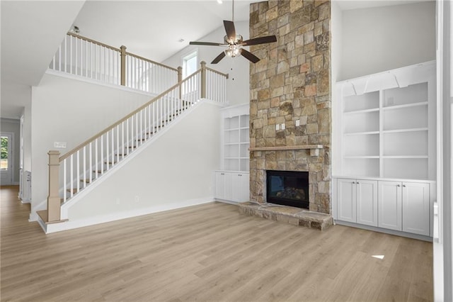 unfurnished living room featuring built in shelves, ceiling fan, a fireplace, and light hardwood / wood-style floors