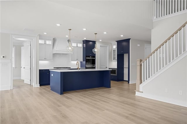 kitchen featuring premium range hood, white cabinetry, a center island with sink, and light hardwood / wood-style flooring