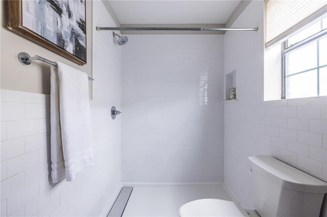 bathroom with a tile shower, tile walls, and toilet