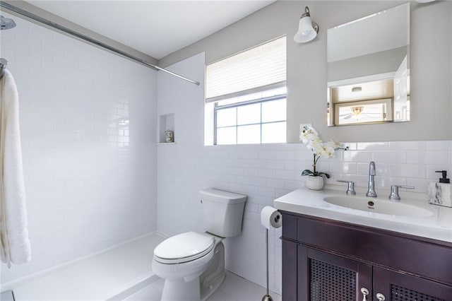 bathroom with tile walls, vanity, toilet, and a tile shower