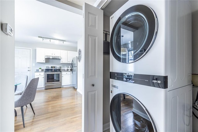 clothes washing area with stacked washer / dryer and light wood-type flooring