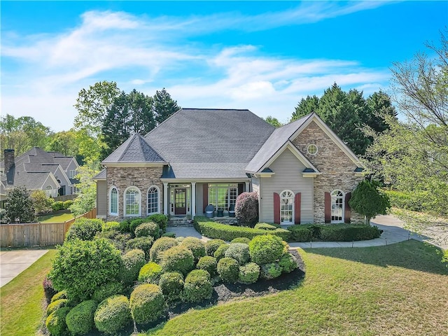 view of front of home featuring a front lawn, stone siding, and fence