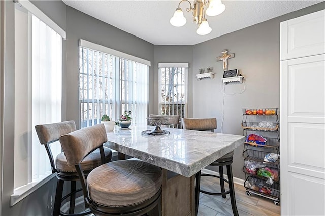 dining room featuring a chandelier, light wood finished floors, a textured ceiling, and baseboards