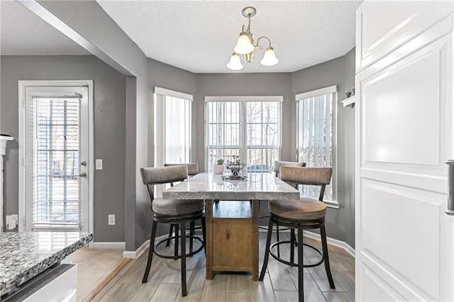 dining space featuring a textured ceiling, plenty of natural light, baseboards, and an inviting chandelier