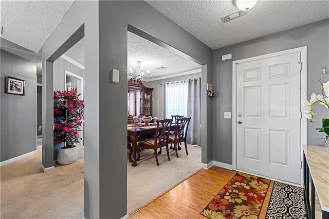 foyer entrance featuring a textured ceiling, a notable chandelier, visible vents, baseboards, and light wood finished floors