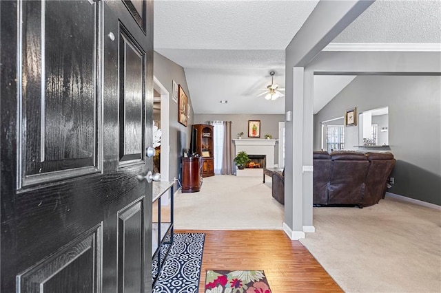 foyer entrance with vaulted ceiling, a warm lit fireplace, light carpet, and a textured ceiling