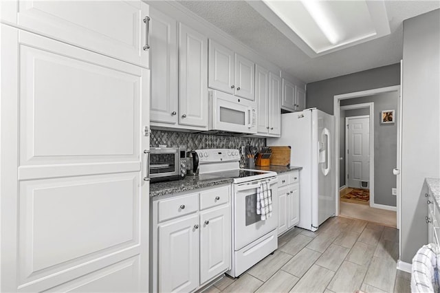 kitchen with a toaster, white appliances, white cabinetry, backsplash, and dark stone countertops