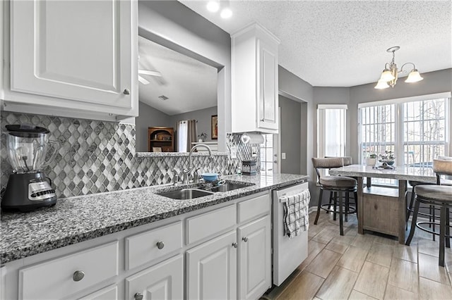 kitchen featuring dishwashing machine, stone counters, a sink, white cabinetry, and backsplash