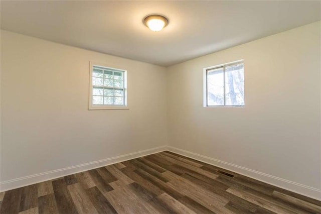 empty room with dark wood-type flooring, a wealth of natural light, and baseboards