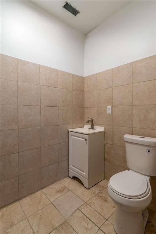 half bath featuring toilet, visible vents, tile walls, and vanity