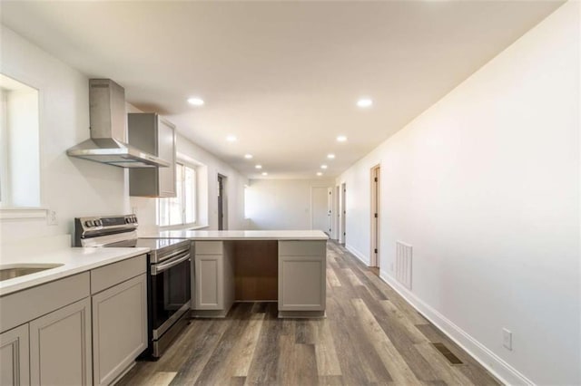 kitchen featuring a peninsula, wall chimney exhaust hood, stainless steel electric stove, and gray cabinetry