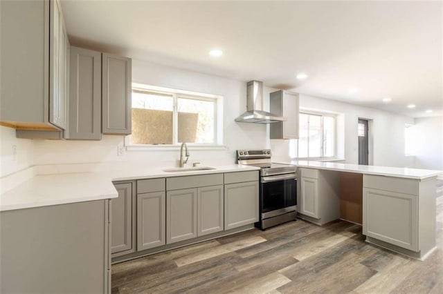 kitchen with gray cabinets, a sink, wall chimney range hood, a peninsula, and stainless steel electric range