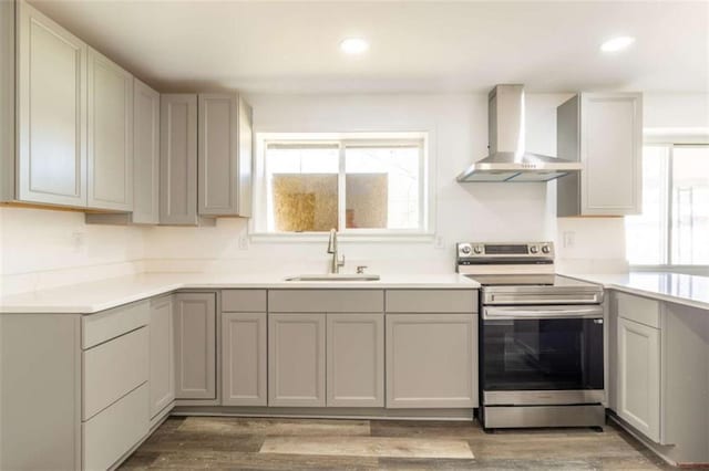 kitchen featuring light wood finished floors, gray cabinetry, a sink, wall chimney range hood, and stainless steel range with electric stovetop