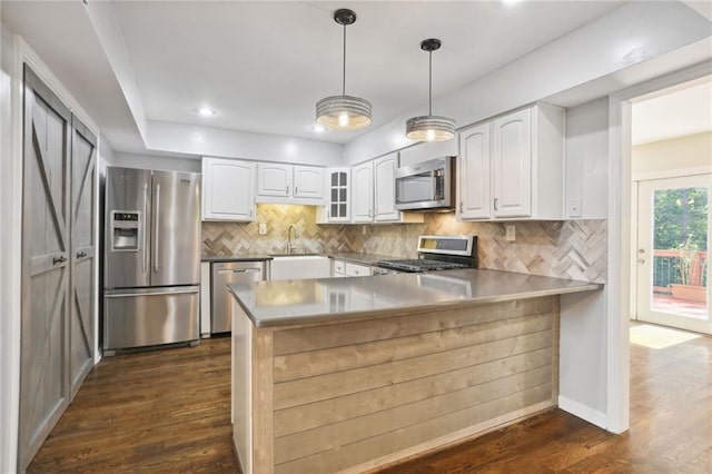 kitchen with kitchen peninsula, appliances with stainless steel finishes, dark wood-type flooring, white cabinetry, and hanging light fixtures