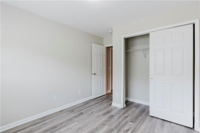 unfurnished bedroom with light wood-style flooring, a closet, and baseboards