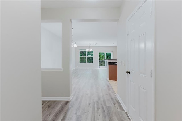 hall featuring light wood-style flooring, a chandelier, and baseboards
