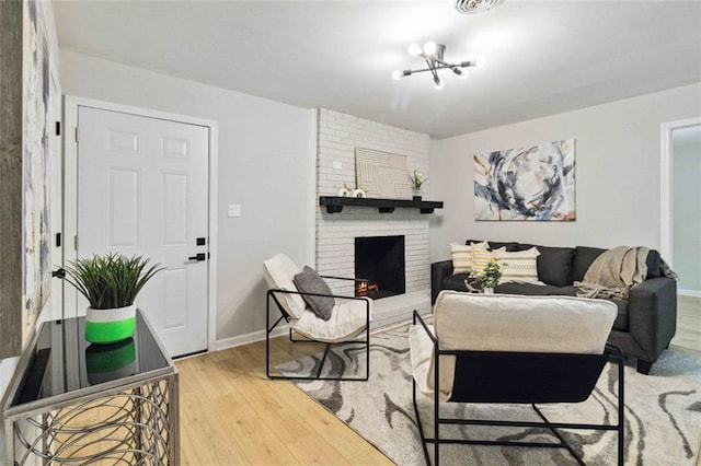 living area with a brick fireplace, a notable chandelier, baseboards, and wood finished floors