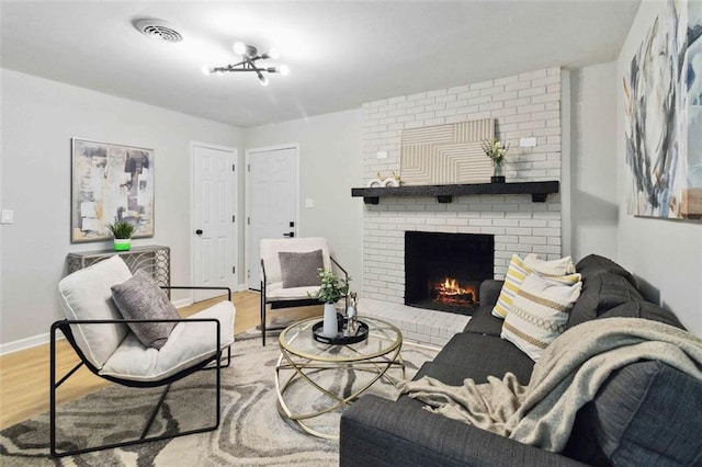 living area featuring a brick fireplace, wood finished floors, visible vents, and baseboards